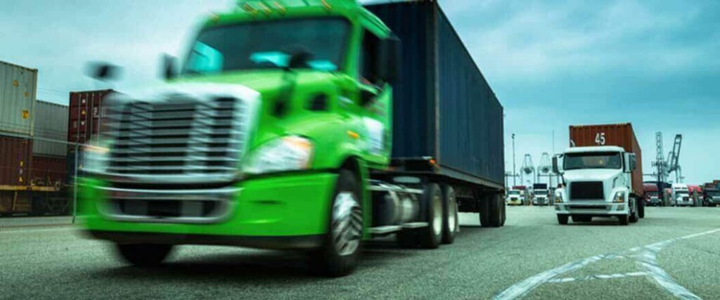 A green semi truck driving away from a port.