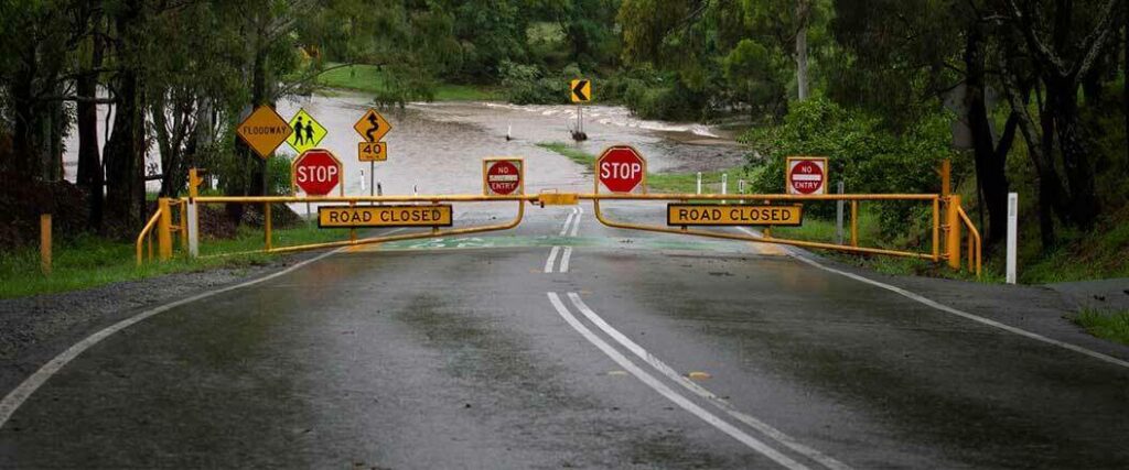 A flooded section of road blocked by a "road closed" gate with stop signs and no entry notifications. 