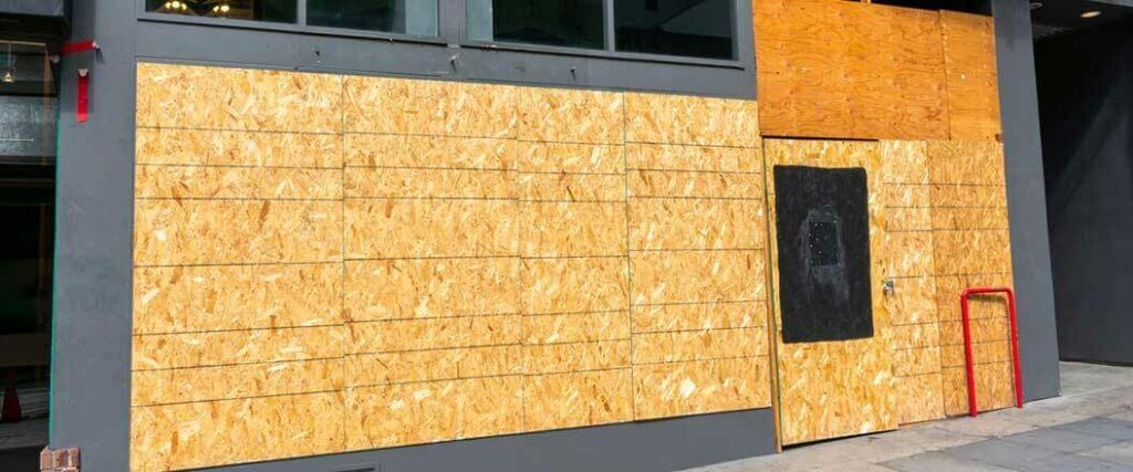 A building with plywood covering vulnerable windows and doors.