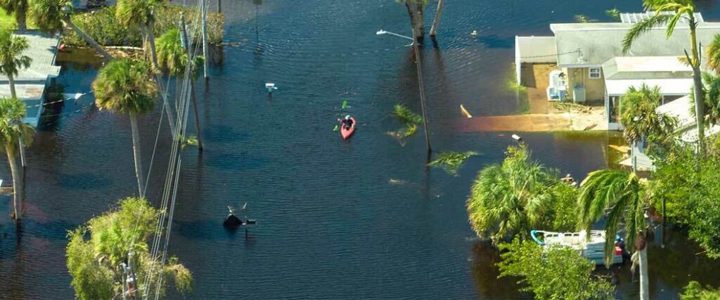 An individual piloting a kayak through a flooded neighborhood.